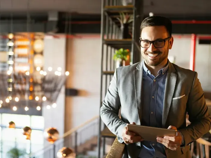 Smiling businessman in a stylish workspace holding a tablet, ready to connect customers with local services
